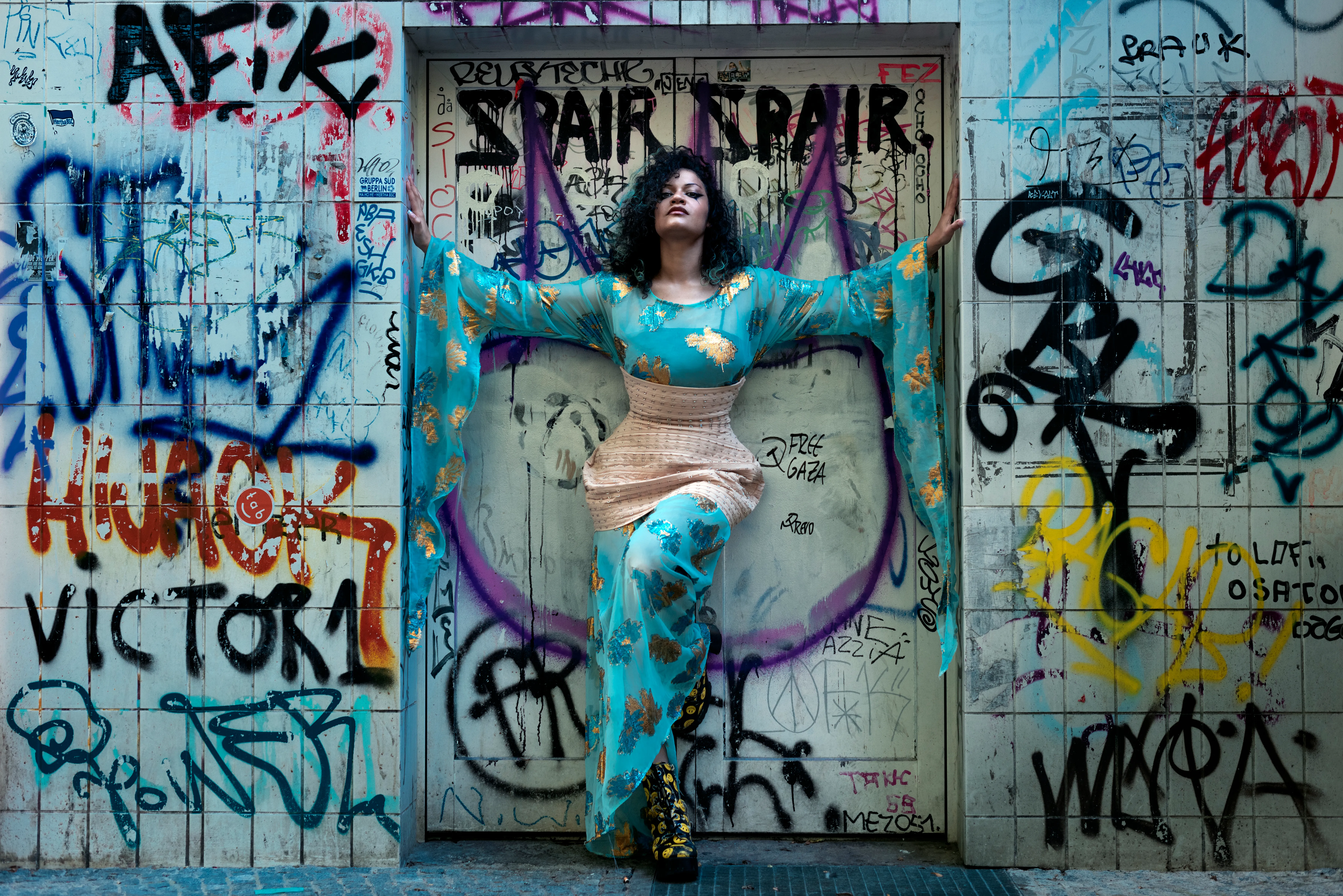 Model wearing a playful dress with shimmering embroidery, photographed in front of graffiti in Berlin.