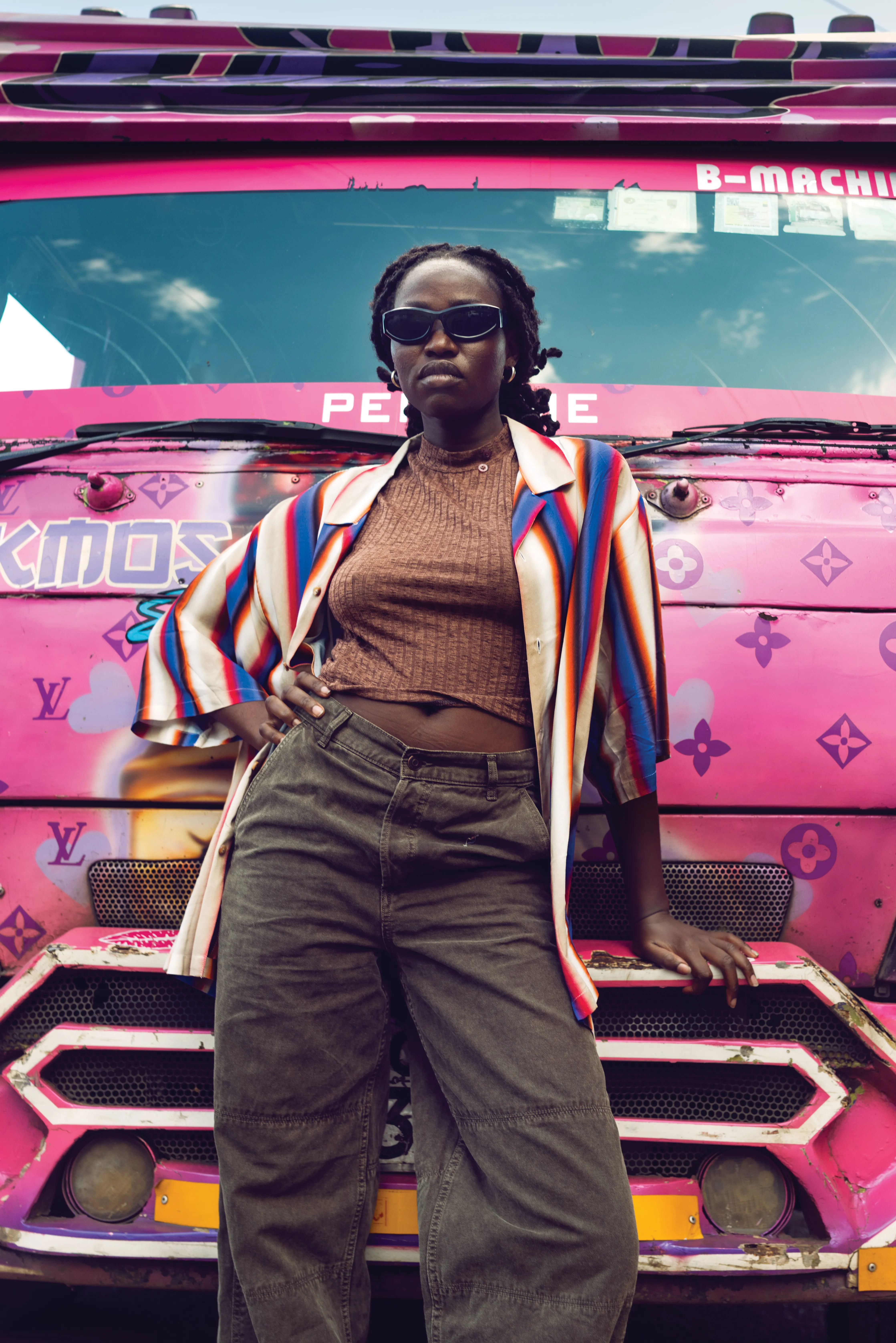 Student from a Kenyan music school posing in front of a colourful Nairobi matatu decorated with an LV-inspired monogram. Creative direction and production by Olya Chuk.