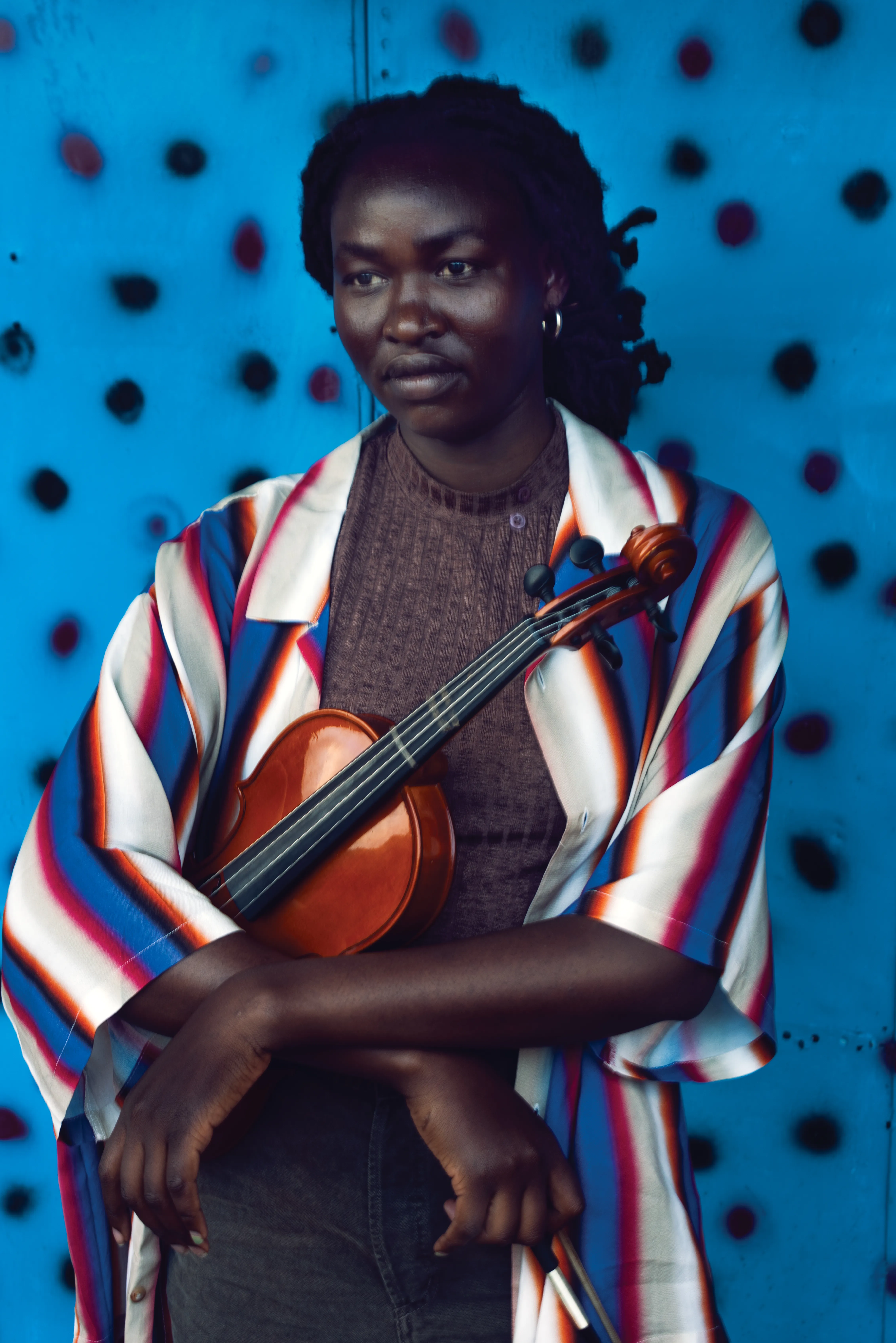 Student from a Kenyan music school holding a violin against an electric blue polka-dot background in Nairobi.