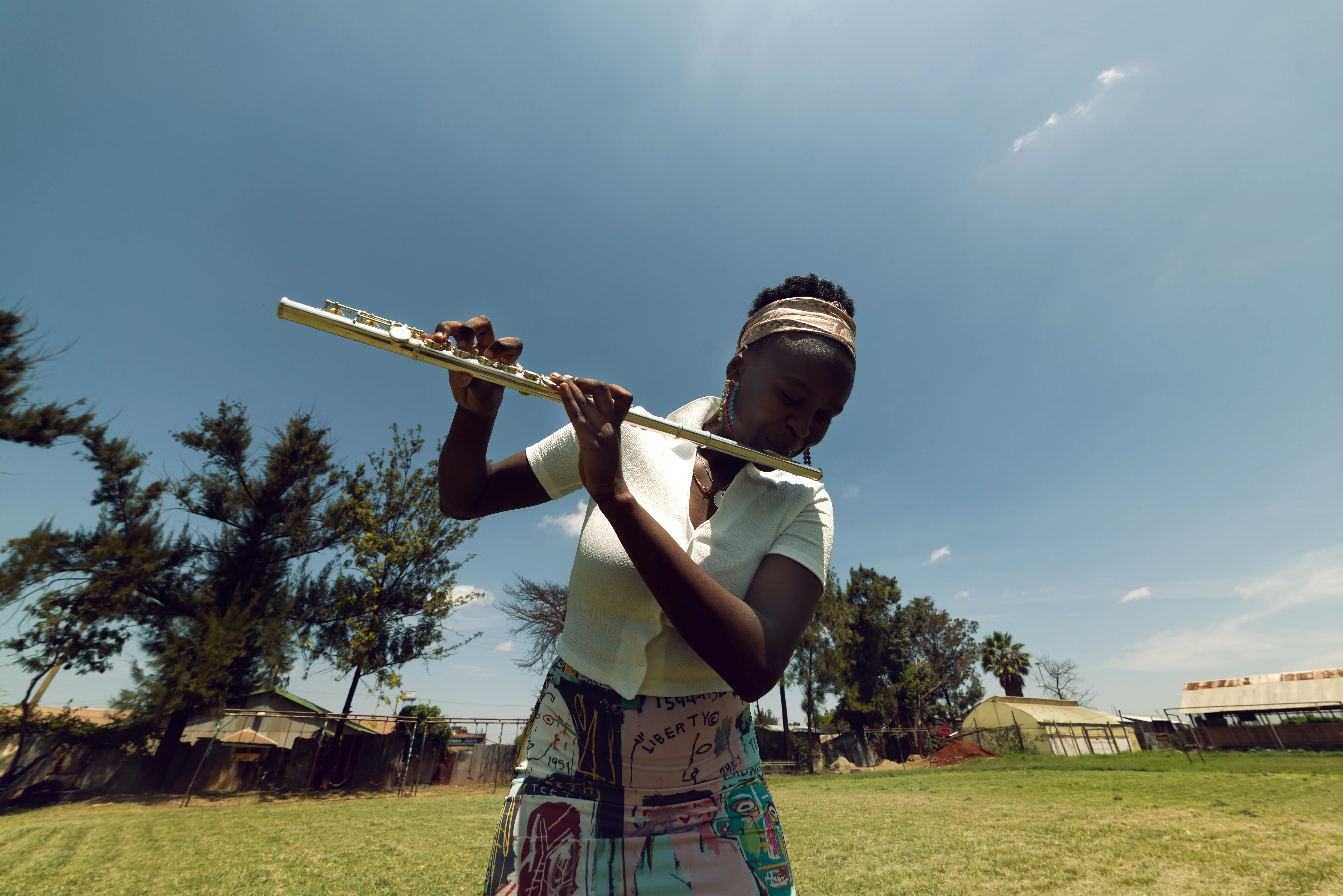 Kenyan music student playing the flute outdoors, wearing a Jean-Michel Basquiat print skirt, styled by Olya Chuk.