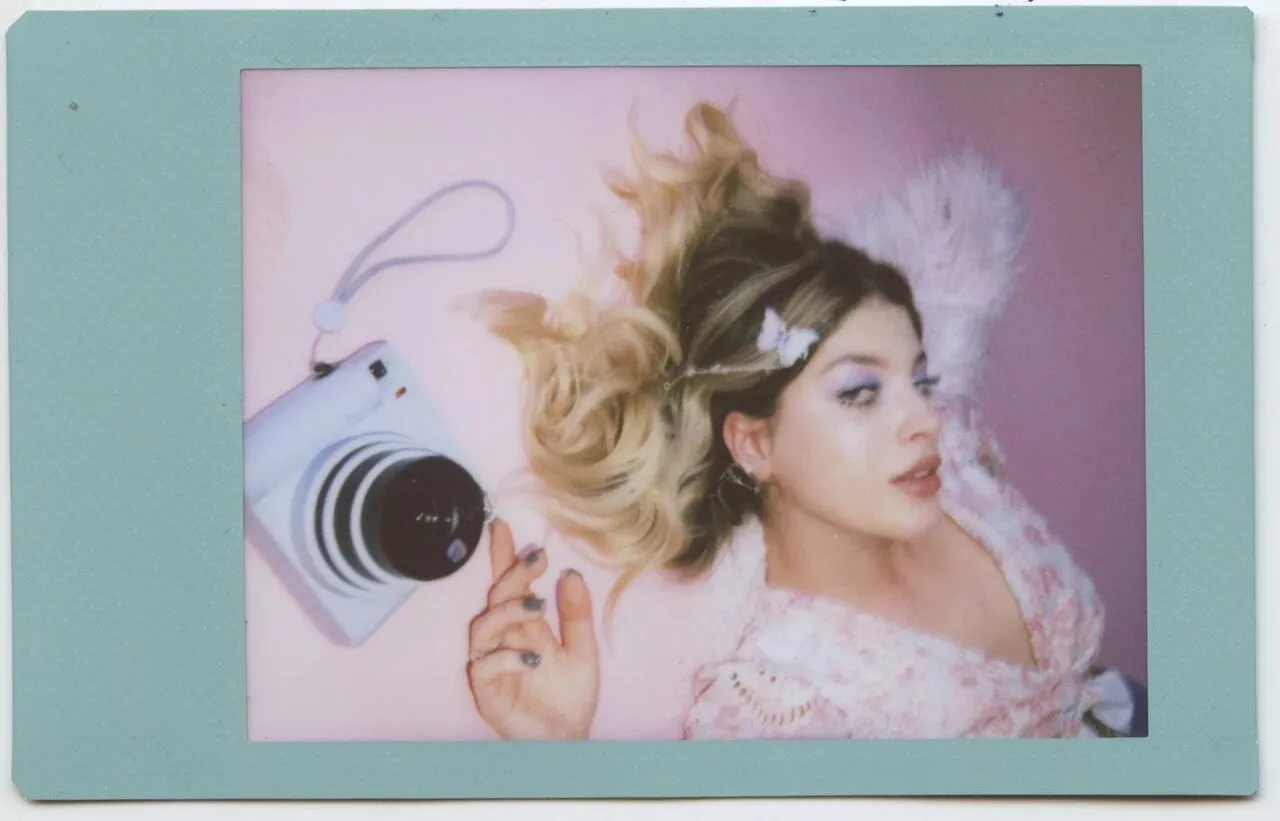 Blogger photographed on Instax for a Vogue × Instax advertorial, wearing a Y2K-inspired sheer top and butterfly headpieces.