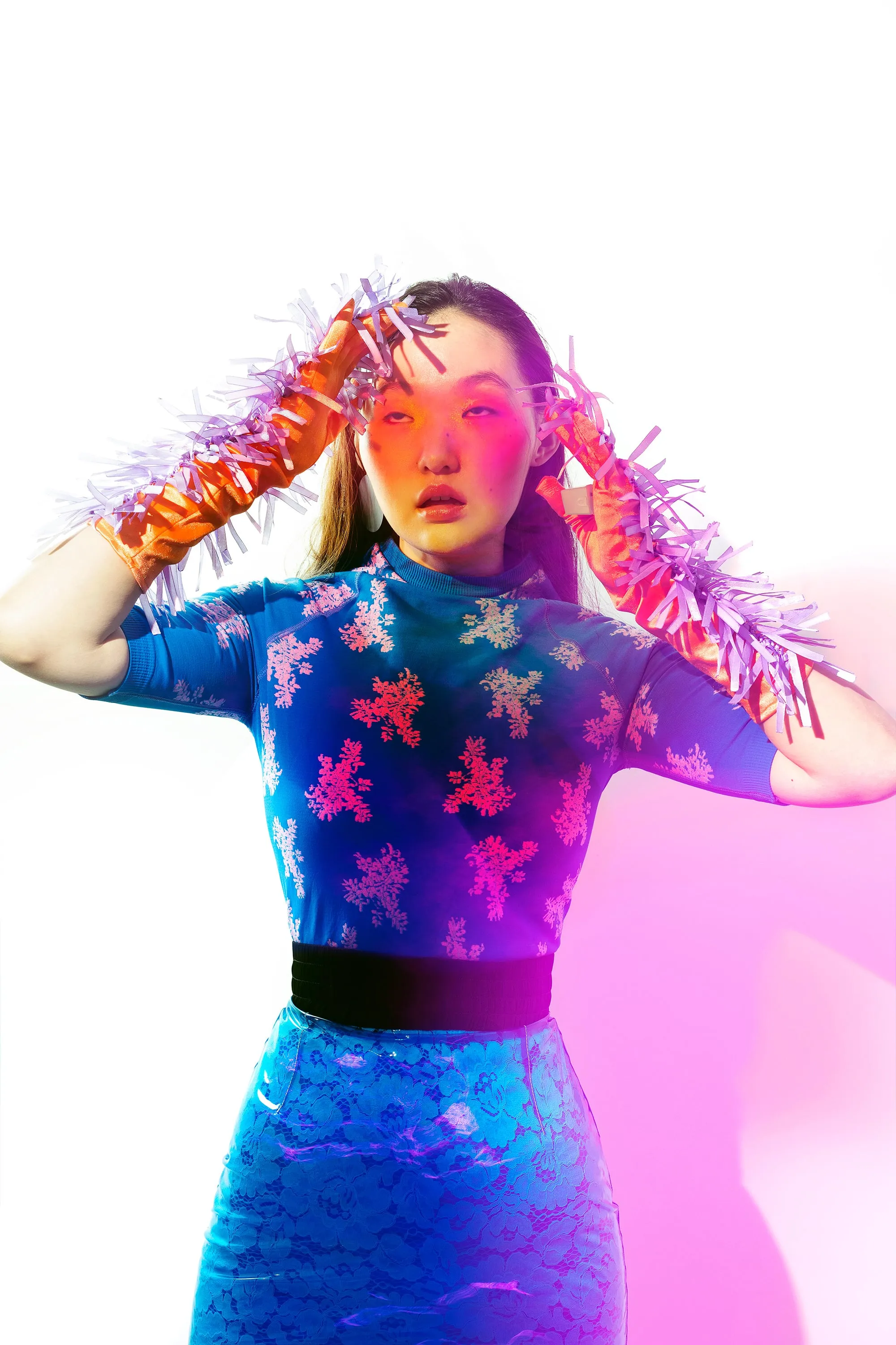 Model wearing a floral dress layered with a transparent blue silicone skirt and bright orange statement gloves.